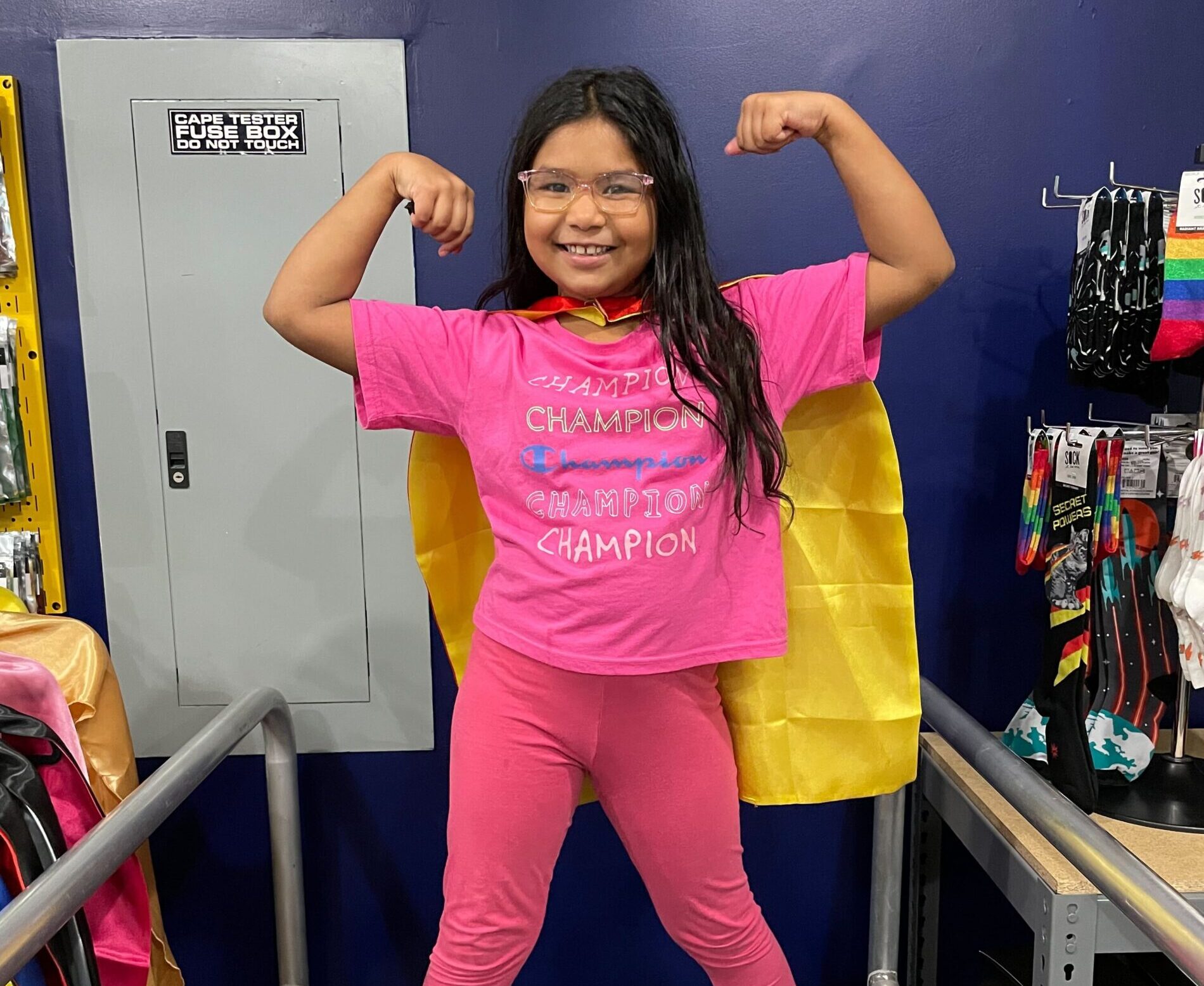 November 2022 Author of the Month Faryal K. poses on the Brooklyn Superhero Supply Co. Cape Tester
