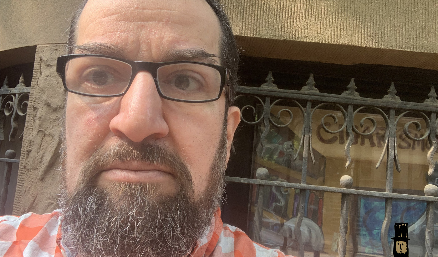 Una selfie de Mike, que tiene barba, anteojos y cabello corto, con una reja de hierro decorativa detrás de él.