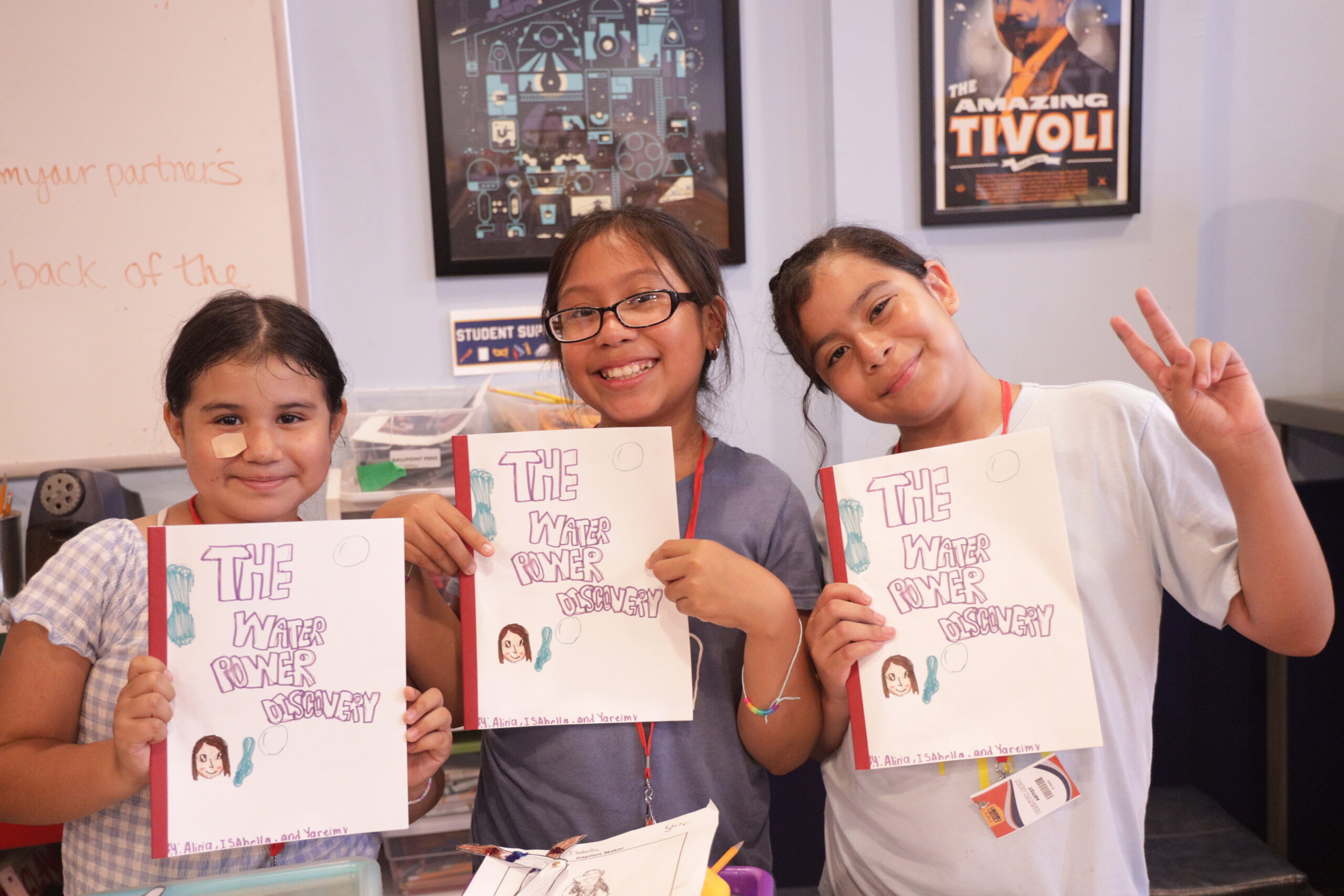 Three students hold up the bound copies of the story they just wrote together, smiling.