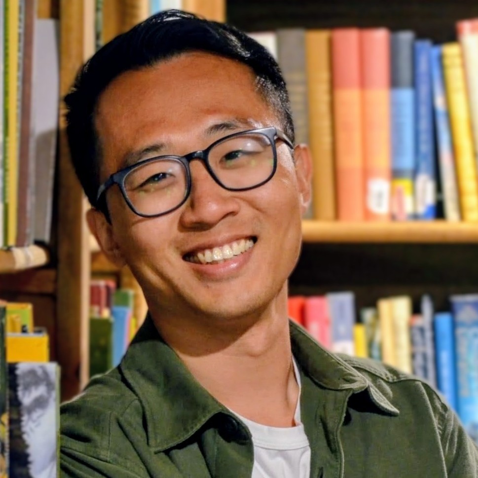 Roger Lam, a man with glasses, smiling in front of bookcases.